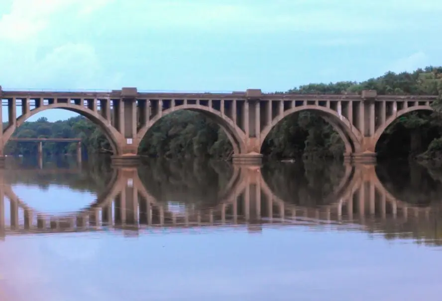 Concrete arch railroad bridge over the Rappahannock River, reflected in still water, seen from the Fredericksburg City Dock